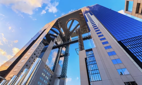 오사카의 랜드마크인 우메다 스카이 빌딩의 거대한 공중 정원 전망대와 기하학적인 유리 외벽이 푸른 하늘과 어우러진 풍경입니다.