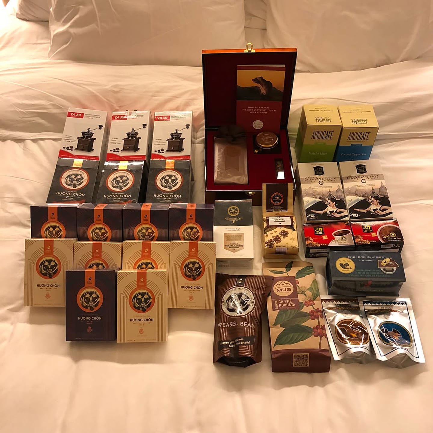 베트남 여행 기념품으로 인기 있는 위즐 커피와 G7 커피 등 다양한 종류의 커피 패키지들이 하얀 침대 위에 가득 펼쳐져 있습니다.