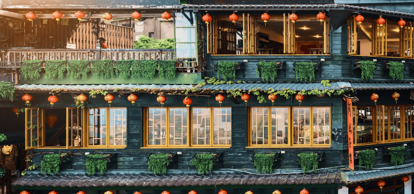 붉은 홍등과 초록색 식물로 장식된 대만 지우펀의 고풍스러운 목조 찻집 건물이 따뜻한 저녁 빛을 머금고 있는 풍경입니다.