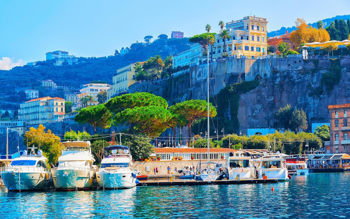 푸른 바다 위 정박한 하얀 요트들과 깎아지른 듯한 절벽 위로 펼쳐진 이탈리아 소렌토의 아름다운 해안 마을 전경입니다.