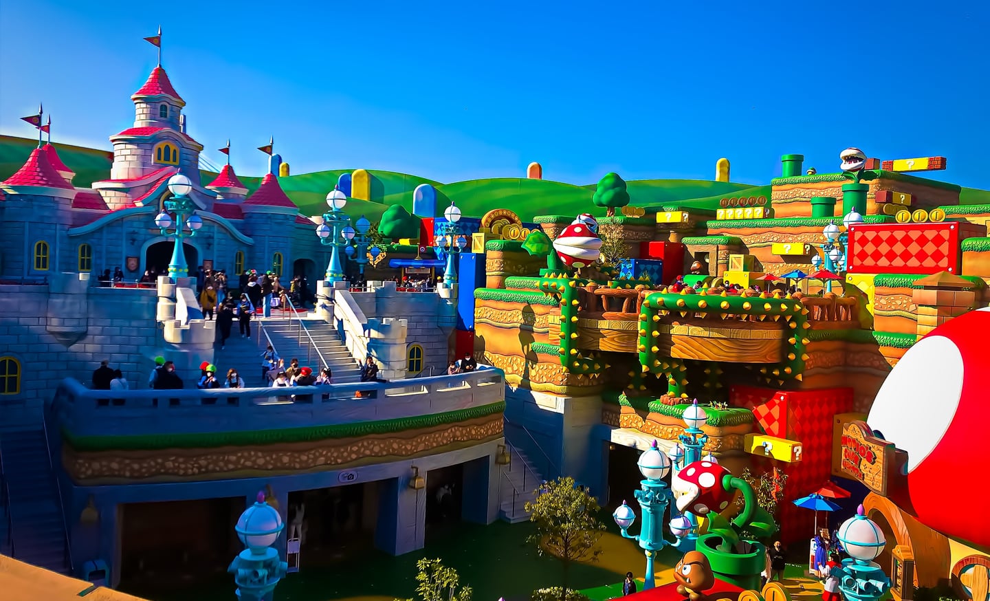 맑은 날씨 속 유니버설 스튜디오 재팬의 슈퍼 닌텐도 월드 전경으로, 피치 성과 게임 속 조형물들이 어우러진 화려한 테마파크 풍경입니다.
