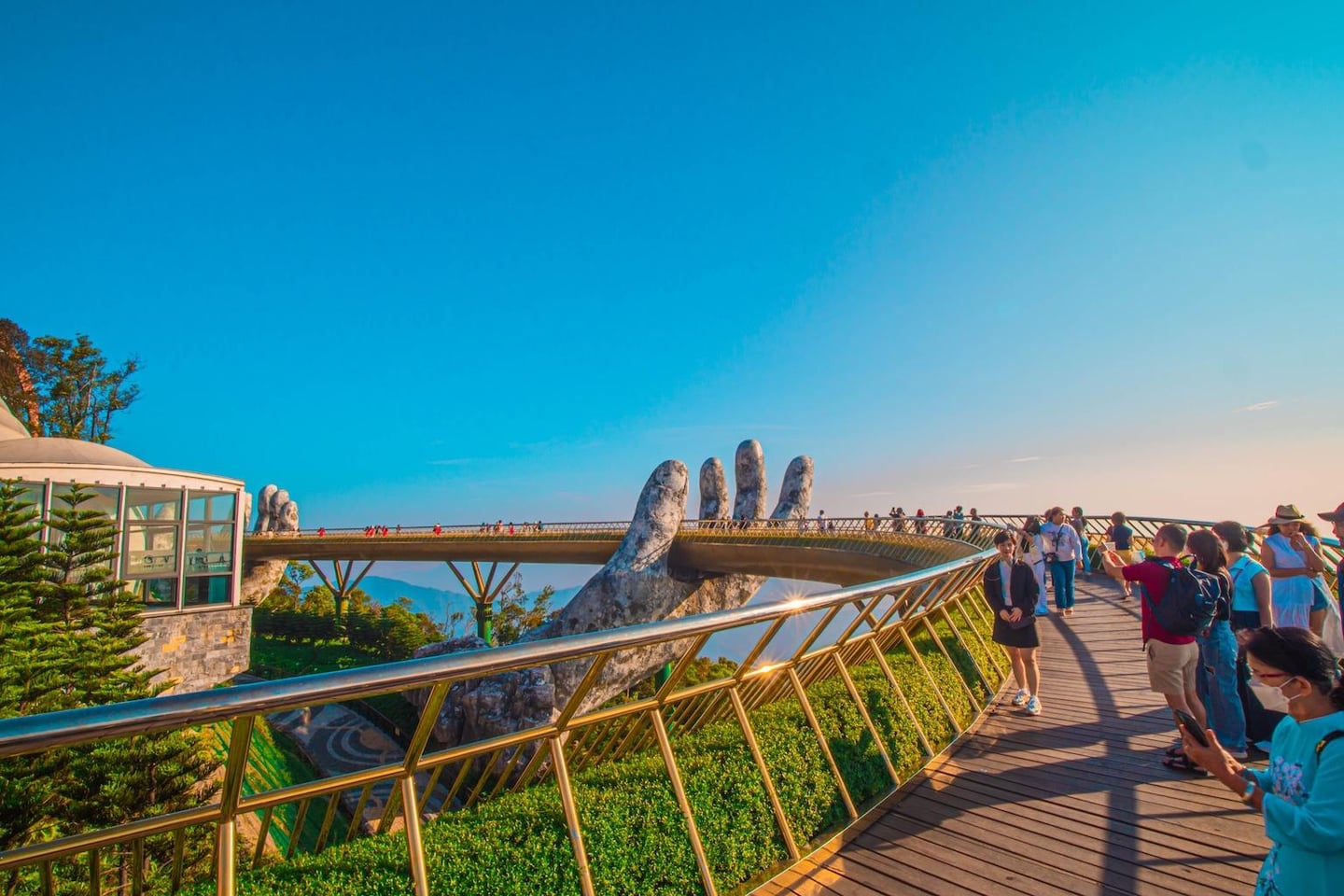 다낭 바나힐의 명소인 골든 브릿지 위에서 거대한 손 조형물과 황금색 난간을 배경으로 기념사진을 찍으며 여유롭게 산책하는 관광객들의 모습입니다.