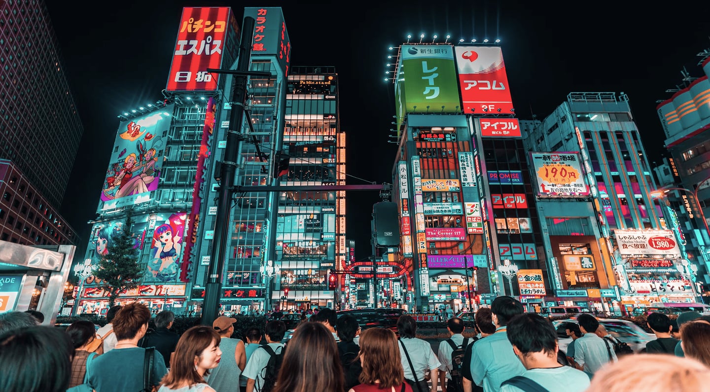 화려한 네온사인과 대형 광고판이 가득한 도쿄 신주쿠 가부키초 거리에서 횡단보도 신호를 기다리는 수많은 사람들의 뒷모습이 담긴 활기찬 야경 사진입니다.