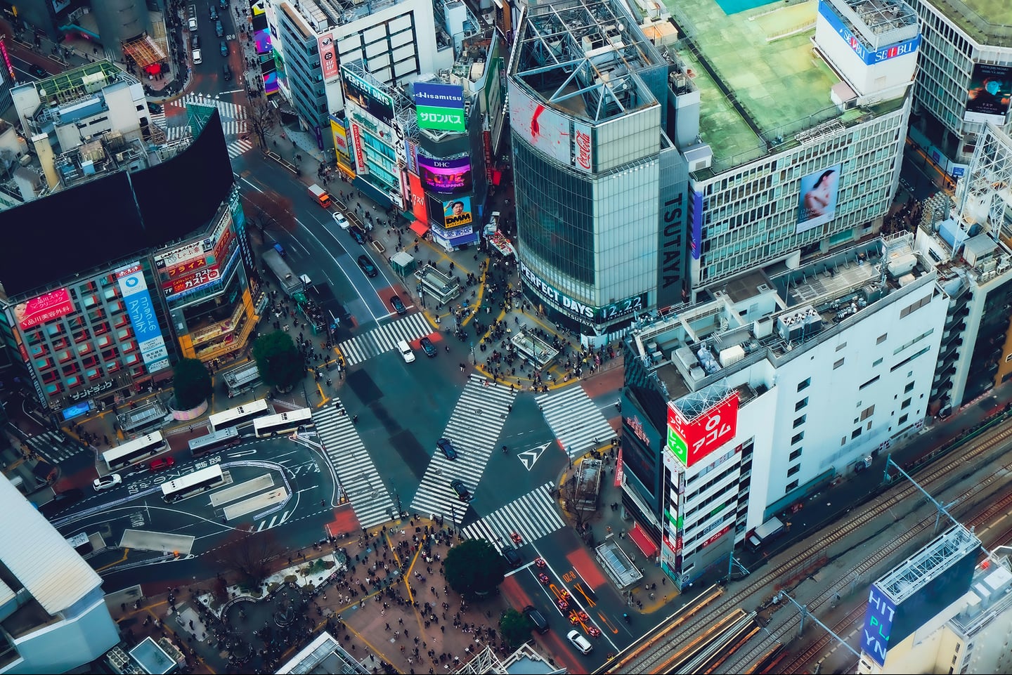 도쿄 시부야의 상징적인 스크램블 교차로를 조망한 사진으로, 횡단보도를 건너는 수많은 사람들과 주변의 화려한 빌딩 숲이 역동적인 도시의 모습을 보여줍니다.