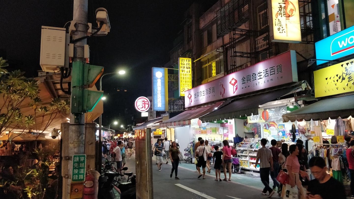 화려한 네온사인 간판이 가득한 대만의 밤거리에서 수많은 인파가 야시장의 상점들을 구경하며 활기차게 걷고 있는 모습입니다.