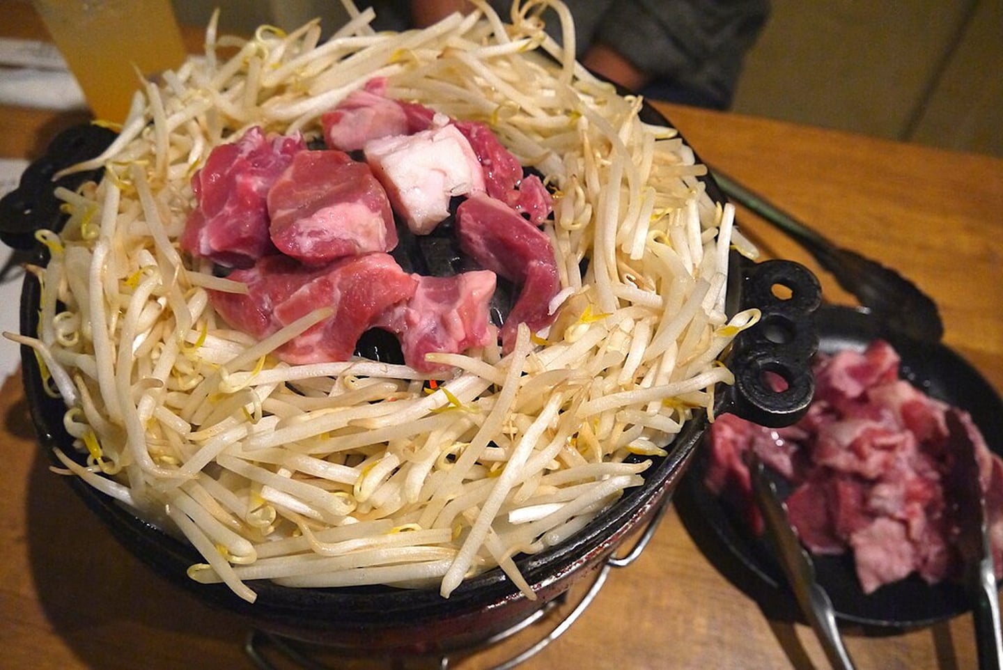 검은색 전용 불판 중앙에 두툼한 양고기를 올리고 주변을 숙주나물로 촘촘하게 둘러 구워 먹는 일본식 징기스칸 구이 요리의 생생한 모습입니다.