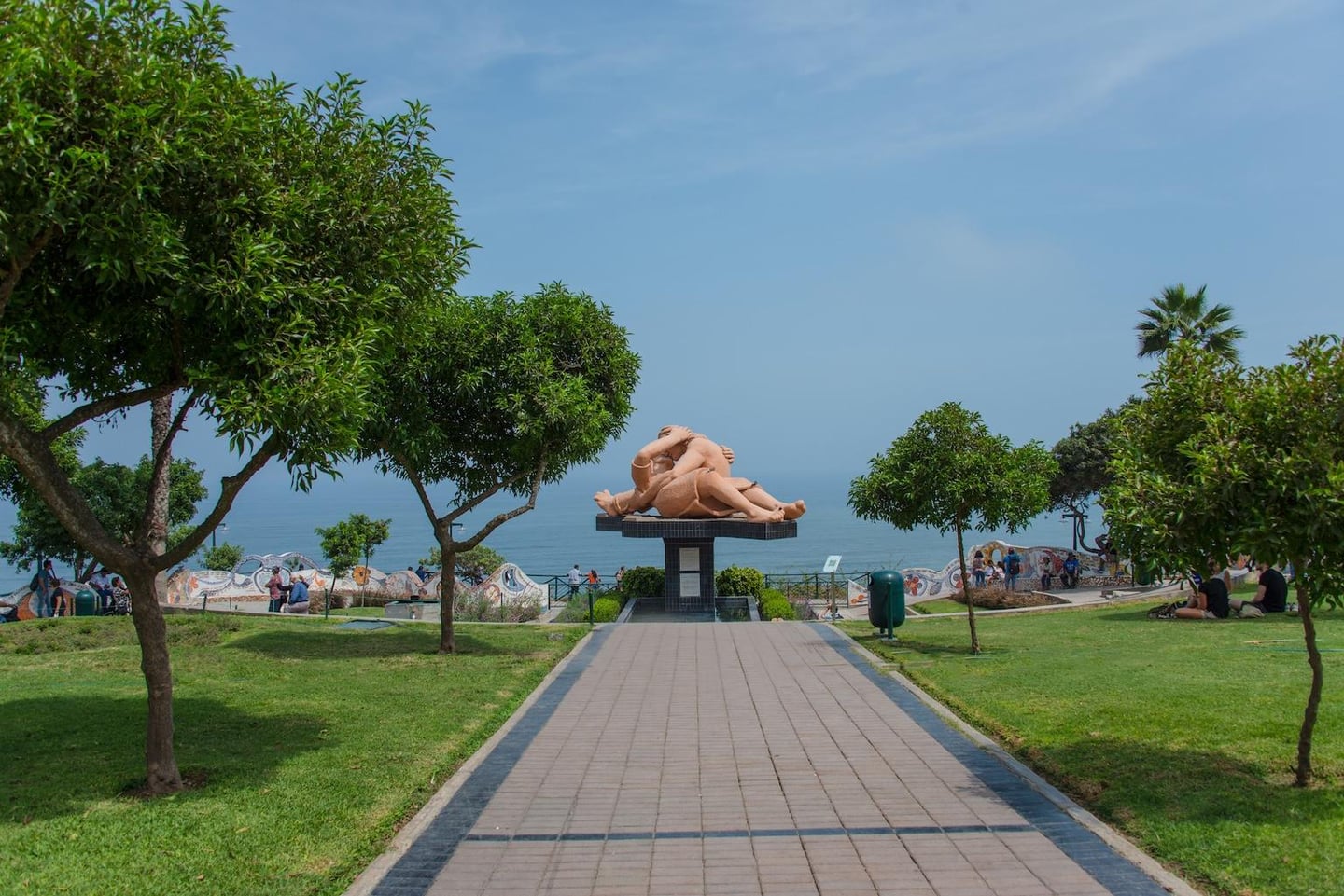 페루 리마의 사랑의 공원에서 바다를 마주보고 서 있는 거대한 연인 조각상과 푸른 잔디밭이 어우러진 산책로의 전경입니다.