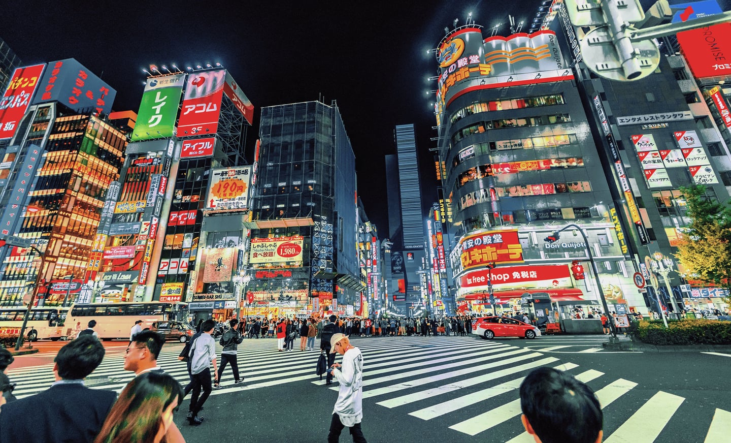 화려한 네온사인과 대형 광고판이 가득한 도쿄 신주쿠 가부키초 거리에서 사람들이 횡단보도를 건너는 역동적인 밤 풍경입니다.