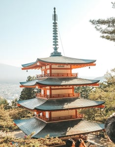 화창한 날씨 속에 우뚝 솟은 붉은색 5층 목조 탑과 그 뒤로 펼쳐진 평화로운 마을 풍경이 어우러진 일본의 전통적인 사찰 전경입니다.