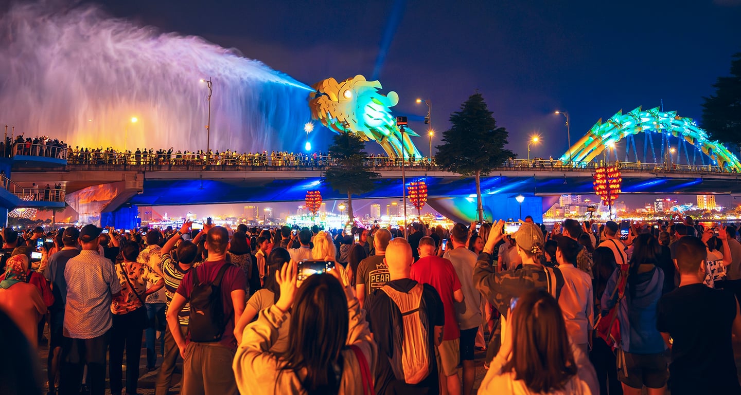 다낭 용다리의 야경 쇼를 보기 위해 모여든 인파와 입에서 거대한 물줄기를 내뿜으며 화려한 조명으로 빛나는 황금빛 용 머리 조형물의 모습입니다.