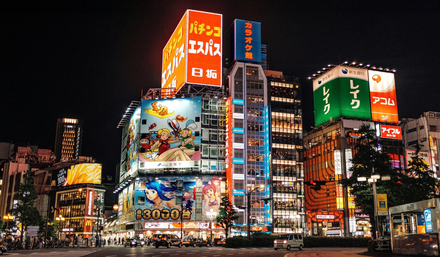 도쿄 신주쿠 가부키초 입구의 화려한 네온사인과 대형 애니메이션 광고판이 가득한 고층 건물들이 늘어선 활기찬 밤거리 풍경입니다.