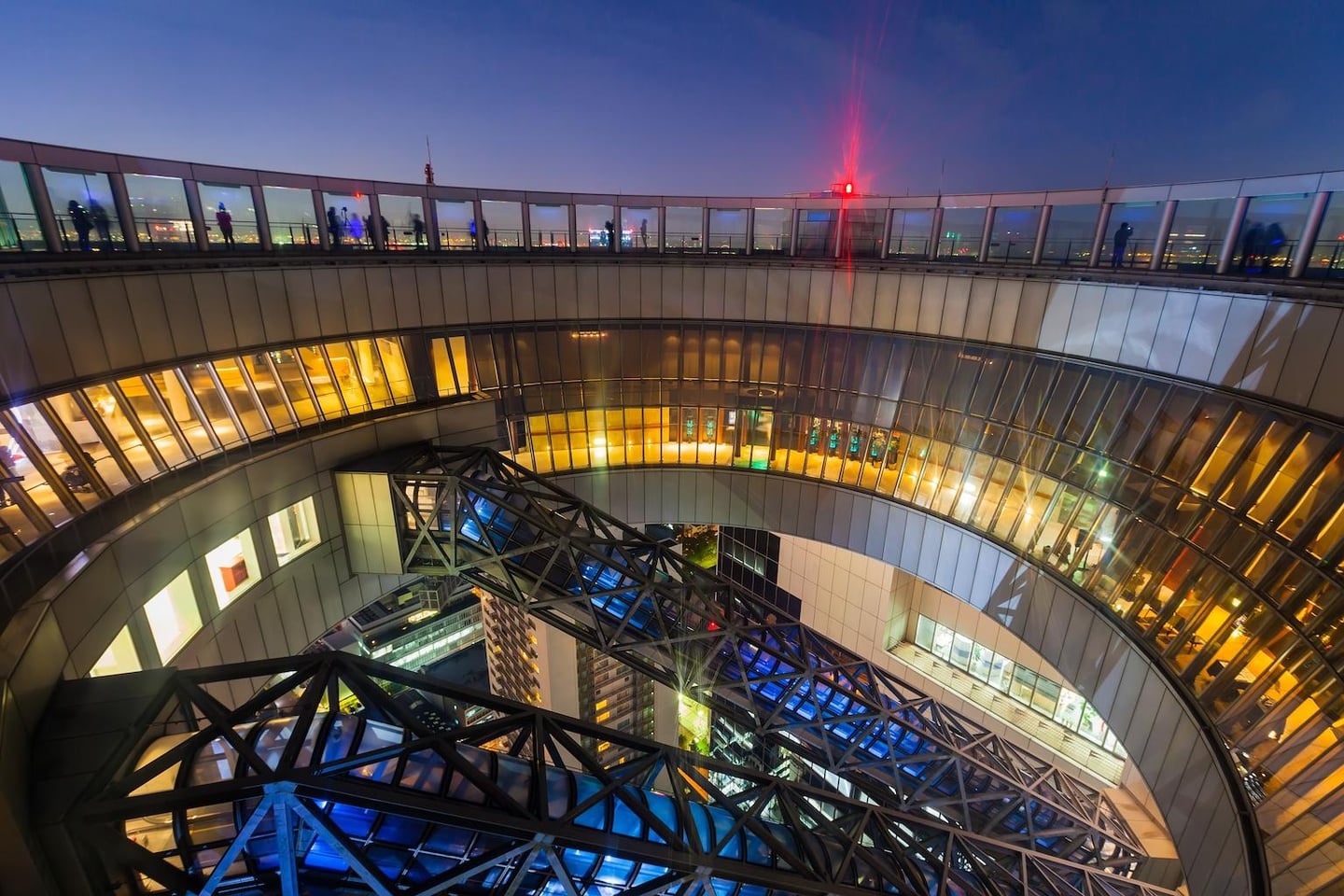 오사카 우메다 스카이 빌딩의 원형 전망대와 공중을 가로지르는 에스컬레이터가 화려한 조명과 어우러진 현대적인 도시 야경 풍경입니다.