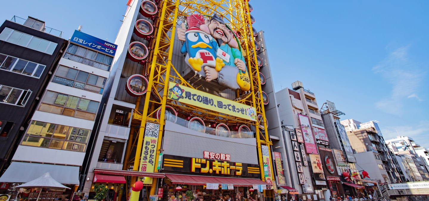 오사카 도톤보리의 랜드마크인 돈키호테 에비스 타워 관람차와 귀여운 캐릭터 조형물이 설치된 화려한 상점가 외관의 모습입니다.