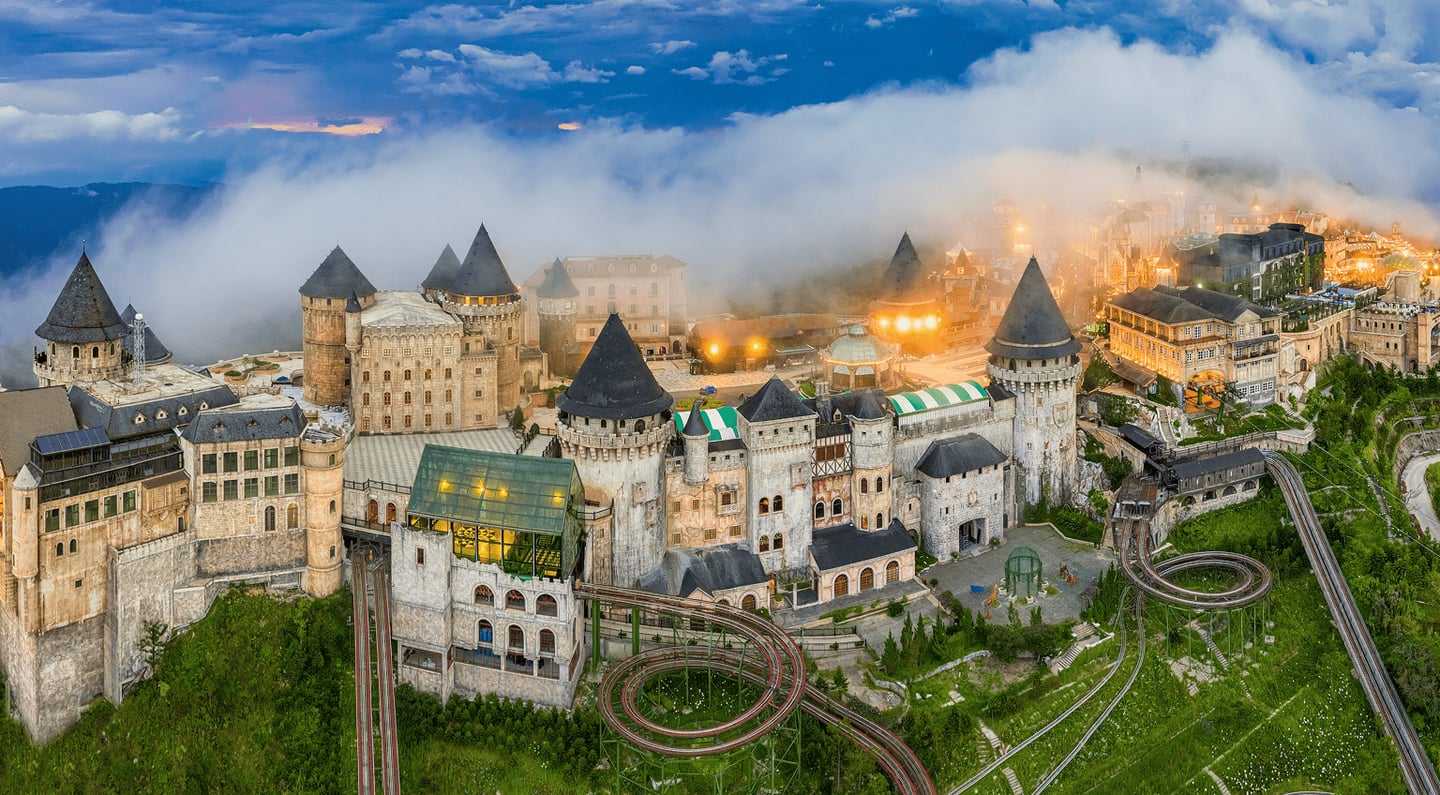 베트남 다낭 바나힐의 안개 낀 산 정상에 위치한 중세 유럽 스타일의 성들과 초록빛 숲 사이로 펼쳐진 루지 트랙의 전경입니다.