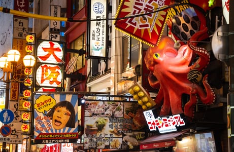 오사카 도톤보리의 상징적인 붉은 문어 간판과 화려한 네온사인, 다양한 음식점 광고판이 가득한 일본의 활기찬 밤거리 풍경입니다.