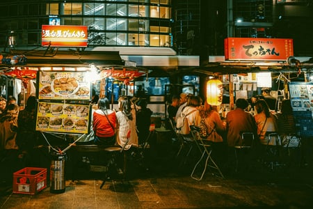 후쿠오카의 밤을 밝히는 야타이 포장마차 거리에 사람들이 옹기종기 모여 앉아 일본 현지 음식을 맛보며 즐거운 시간을 보내는 풍경입니다.