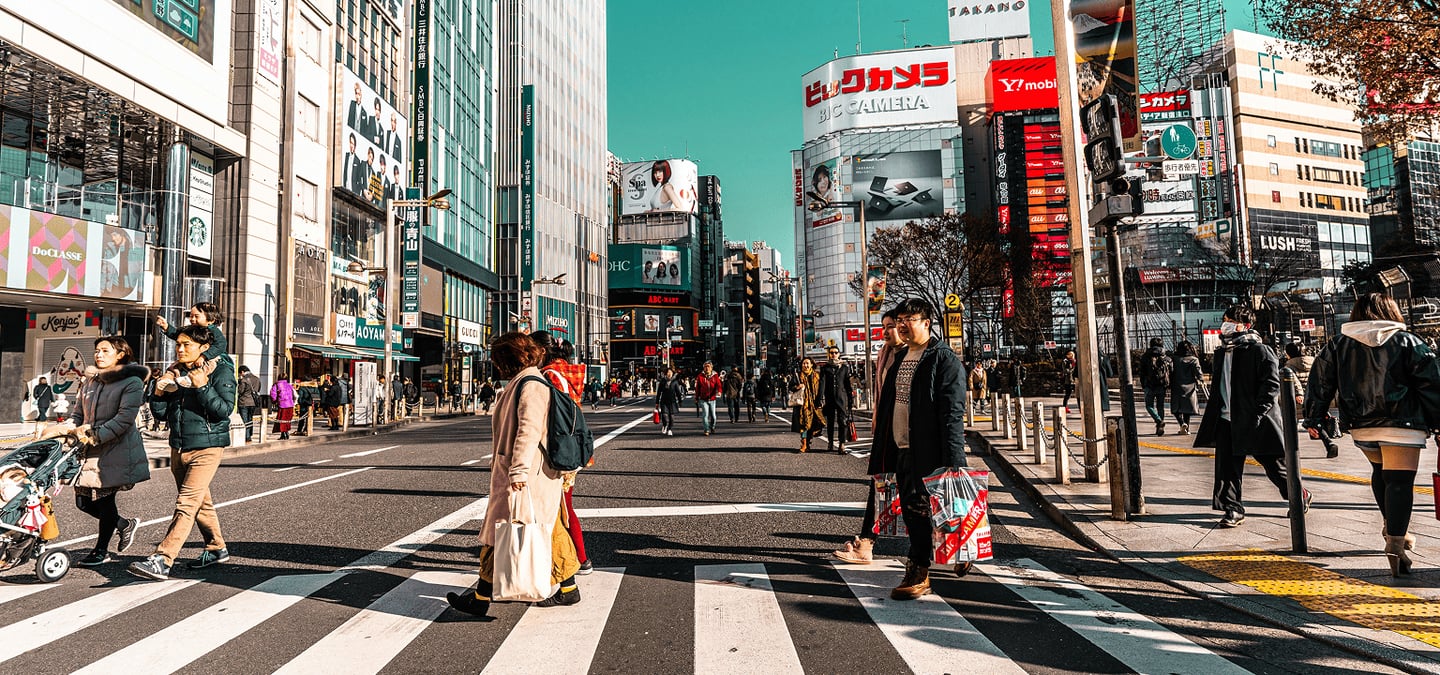 도쿄 신주쿠의 고층 빌딩과 화려한 간판이 가득한 거리에서 횡단보도를 건너는 사람들과 활기찬 도심의 낮 풍경