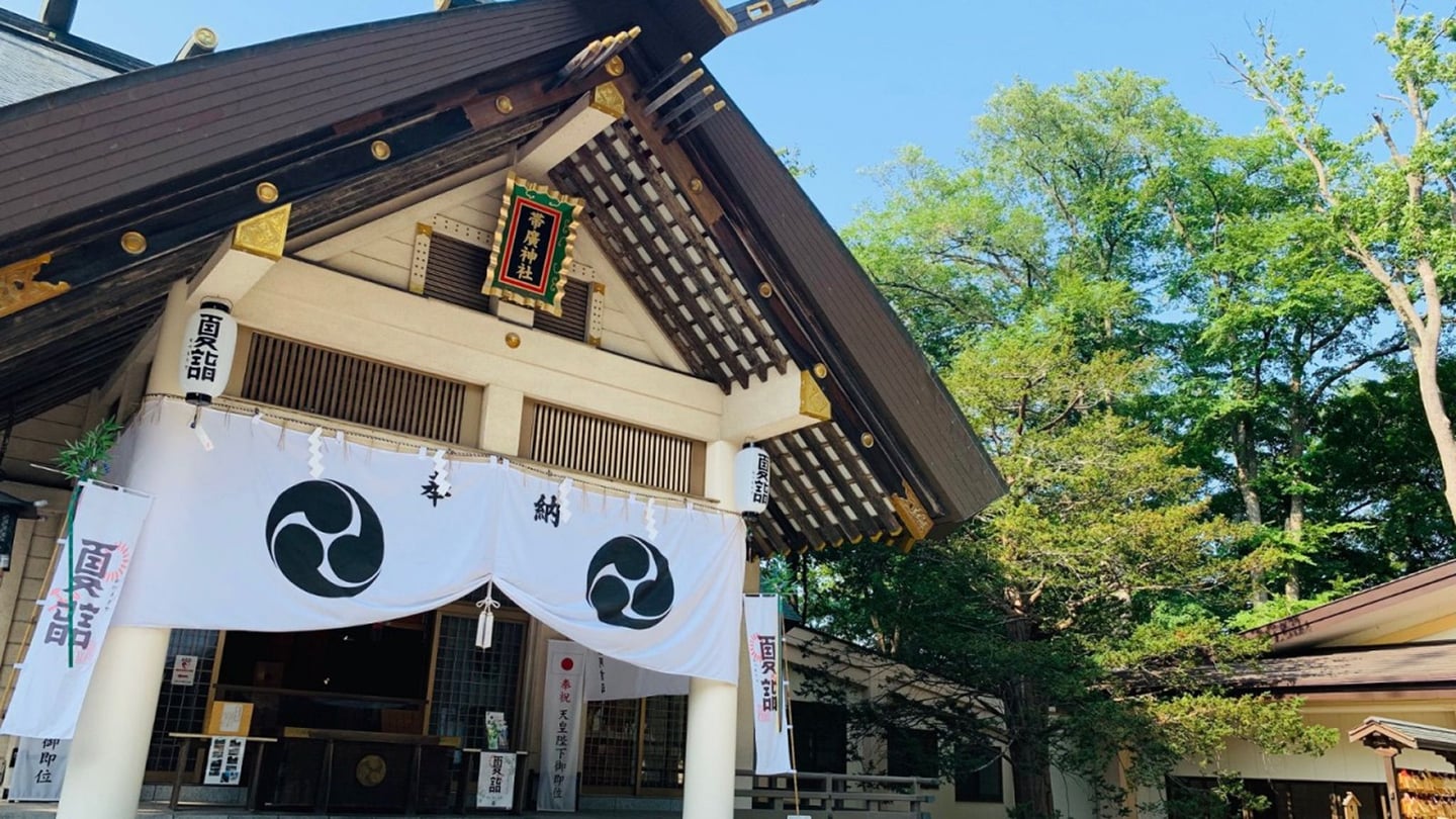 울창한 숲을 배경으로 세워진 일본 전통 신사의 목조 지붕과 흰색 휘장이 어우러진 평화로운 풍경입니다.