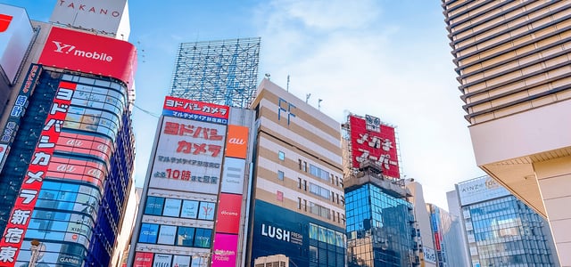 도쿄 신주쿠 도심 속 요도바시 카메라와 러쉬 등 다양한 브랜드의 대형 광고판이 부착된 고층 빌딩들이 늘어선 화려한 거리 풍경