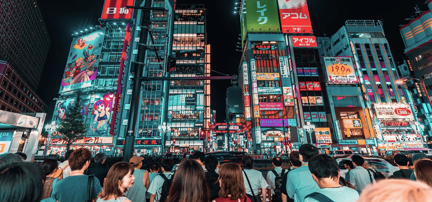 화려한 네온사인과 애니메이션 광고판이 빛나는 도쿄 신주쿠 가부키초 입구에서 신호를 기다리는 인파의 역동적인 밤거리 모습입니다.