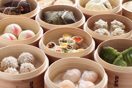 대나무 찜기 속에 담긴 알록달록한 딤섬과 만두, 연잎밥 등 다채로운 종류의 홍콩식 요리가 테이블 위에 가득 차 있는 모습입니다.
