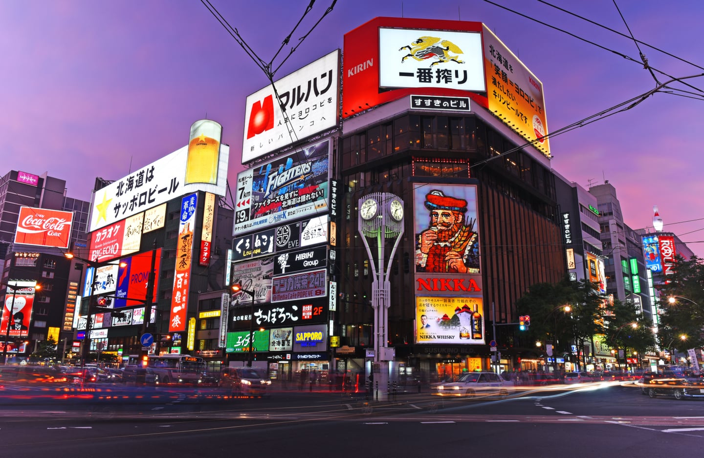 보랏빛 하늘 아래 니카 위스키와 기린 맥주 등 화려한 네온사인 광고판이 빛나는 삿포로 스스키노 거리의 역동적인 야경 모습입니다.