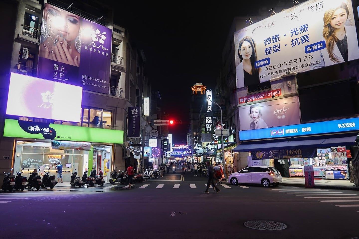 화려한 대형 광고판과 네온사인이 가득한 대만의 밤거리에서 사람들이 횡단보도를 건너고 오토바이가 주차된 활기찬 도심 풍경입니다.