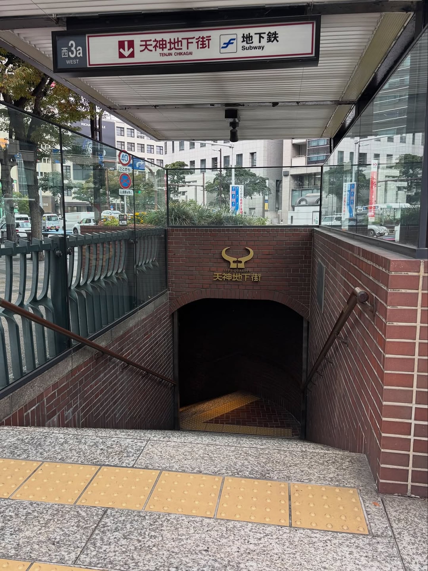 붉은 벽돌로 꾸며진 후쿠오카 텐진 지하상가 입구 계단과 상단에 걸린 일본어 및 영어 안내 표지판의 전경입니다.