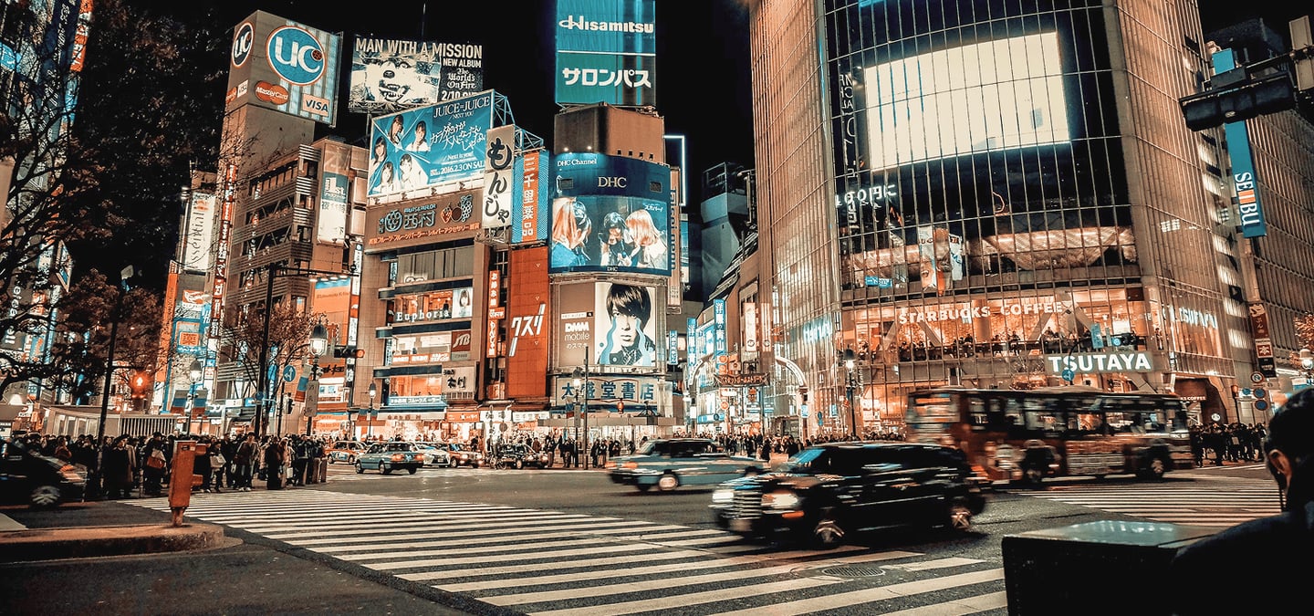 화려한 네온사인과 대형 전광판이 가득한 도쿄 시부야의 밤거리에서 차량들이 횡단보도를 가로지르며 달리는 역동적인 도심 야경 모습입니다.