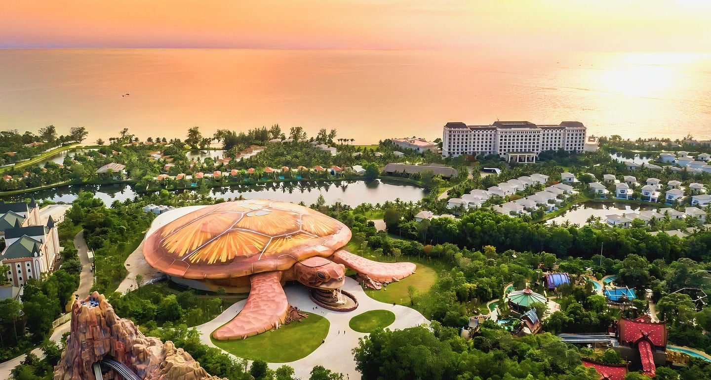 황금빛 노을이 내리는 해변 리조트 단지 중앙에 거대한 거북이 형상의 대형 아쿠아리움 건물이 숲과 호수에 둘러싸여 있는 이색적인 풍경입니다.