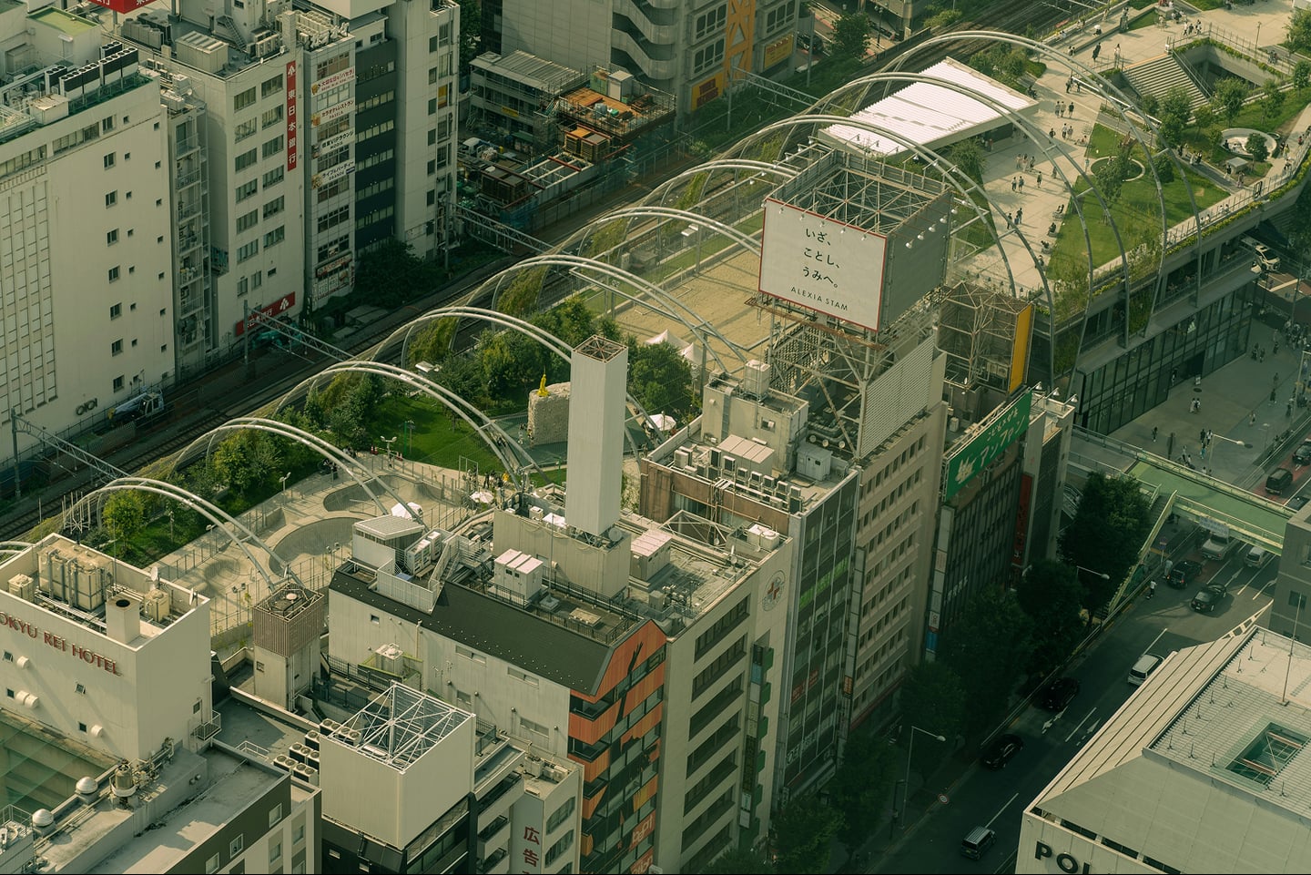 도쿄 시부야 미야시타 공원의 독특한 아치형 철골 구조물과 주변 빌딩 숲이 어우러진 도심의 전경을 높은 시점에서 촬영한 모습입니다.