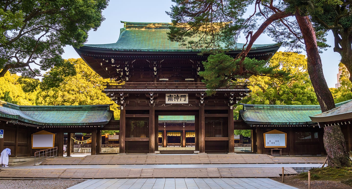 울창한 숲속에 자리 잡은 웅장한 목조 양식의 메이지 신궁 남신문이 푸른 지붕과 정교한 건축미를 뽐내며 서 있는 모습입니다.