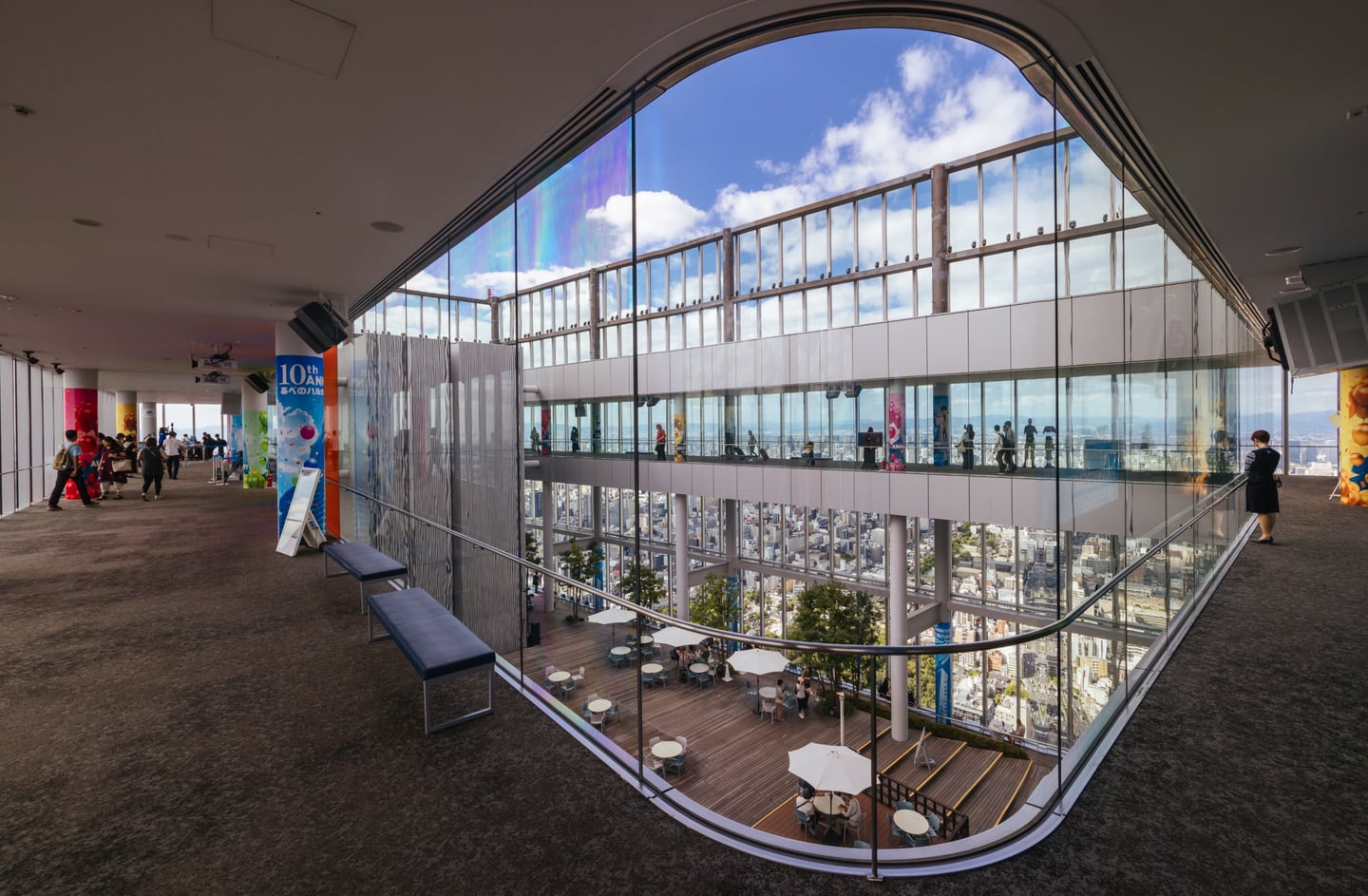 탁 트인 통유리창 너머로 도심 풍경이 펼쳐지는 고층 빌딩 전망대 내부와 야외 테라스 카페의 평화로운 모습입니다.