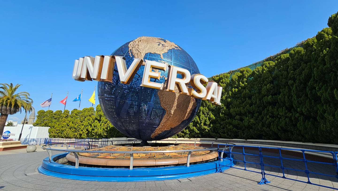 쾌청한 날씨 속 유니버설 스튜디오 재팬 입구에 위치한 거대한 회전 지구본 조형물과 주변의 푸른 나무들이 어우러진 풍경입니다.