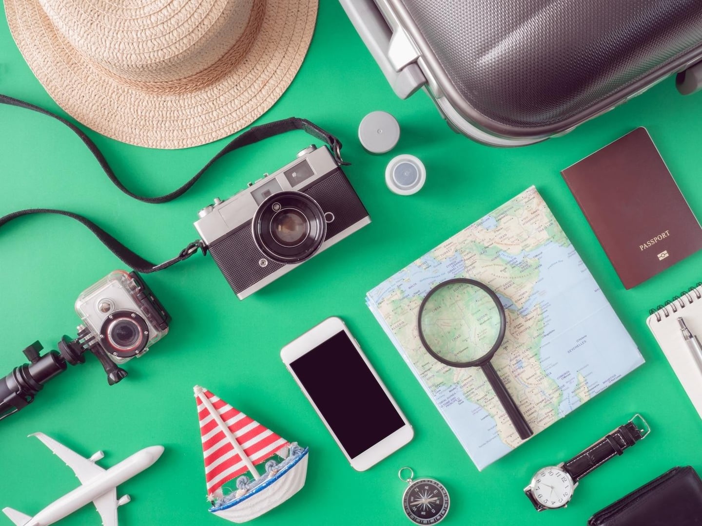 민트색 바탕에 놓인 카메라, 지도, 여권, 스마트폰과 여행용 캐리어 등 다채로운 여행 소품들이 조화롭게 어우러진 평면 구성 사진입니다.