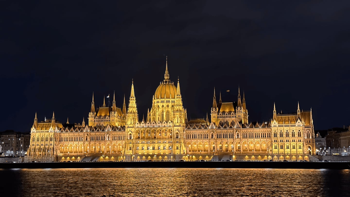 밤하늘을 배경으로 황금빛 조명이 켜진 웅장한 부다페스트 국회의사당 건물이 다뉴브 강변을 따라 화려하게 펼쳐진 모습입니다.