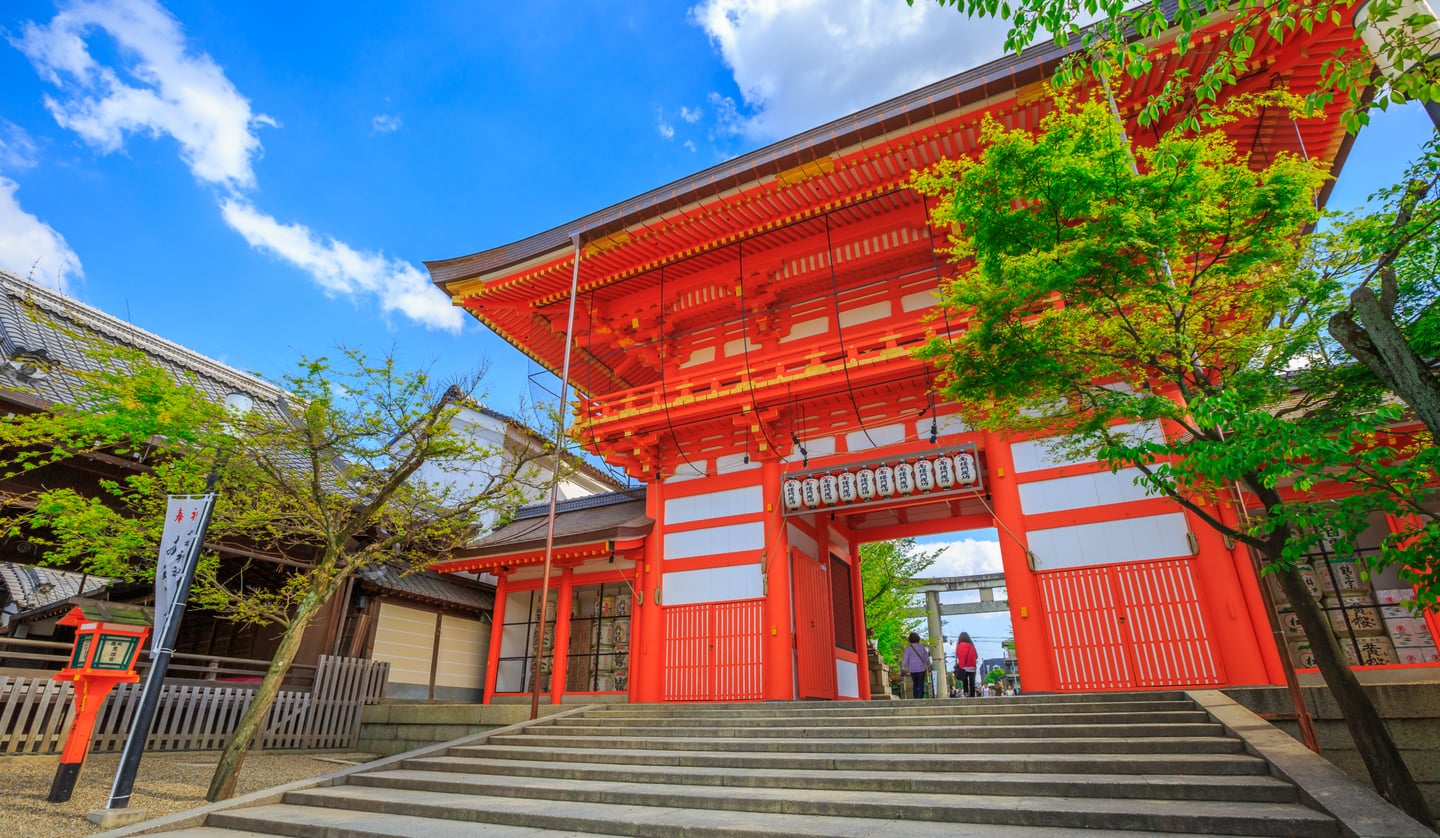 맑은 날씨 속에서 화려한 주황색 목조 건축물로 이루어진 일본 신사의 정문과 그 앞으로 길게 이어진 돌계단의 풍경입니다.
