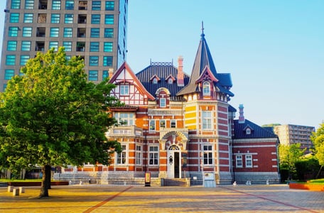 현대적인 고층 빌딩을 배경으로 붉은 벽돌과 뾰족한 지붕이 돋보이는 고전적인 양식의 도서관 건물이 넓은 광장 옆에 자리 잡고 있습니다.