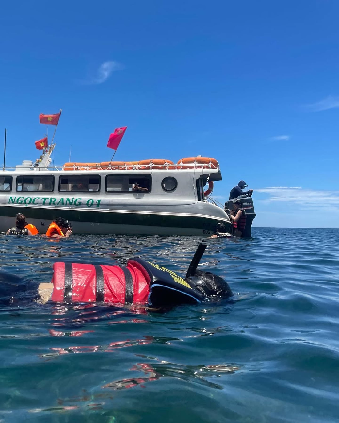 푸른 바다 위에서 구명조끼와 스노클 장비를 착용하고 수영하는 사람들과 베트남 국기가 펄럭이는 하얀색 관광 보트의 풍경입니다.
