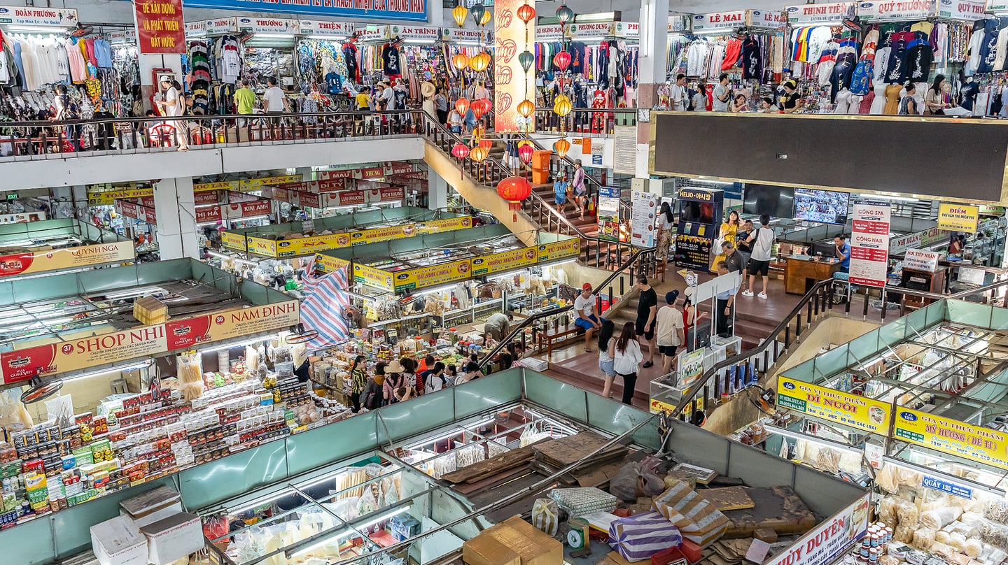 다양한 상점과 인파로 북적이는 베트남 다낭 한 시장의 실내 모습으로 화려한 등불과 빽빽하게 들어선 매대들이 활기찬 전통 시장의 풍경을 보여줍니다.