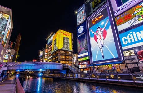 오사카 도톤보리의 상징인 글리코상 전광판과 아사히 맥주 광고가 화려하게 빛나는 운하 주변의 역동적인 밤 거리 풍경입니다.