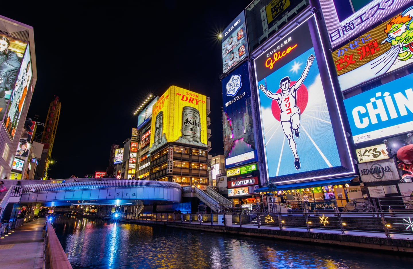 오사카 도톤보리의 상징인 글리코상 전광판과 아사히 맥주 광고가 화려하게 빛나는 운하 주변의 역동적인 밤 거리 풍경입니다.