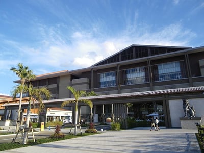 맑은 날씨 속 야자수가 심어진 넓은 광장과 세련된 디자인의 대형 리조트 건물이 조화를 이루는 평화로운 전경입니다.