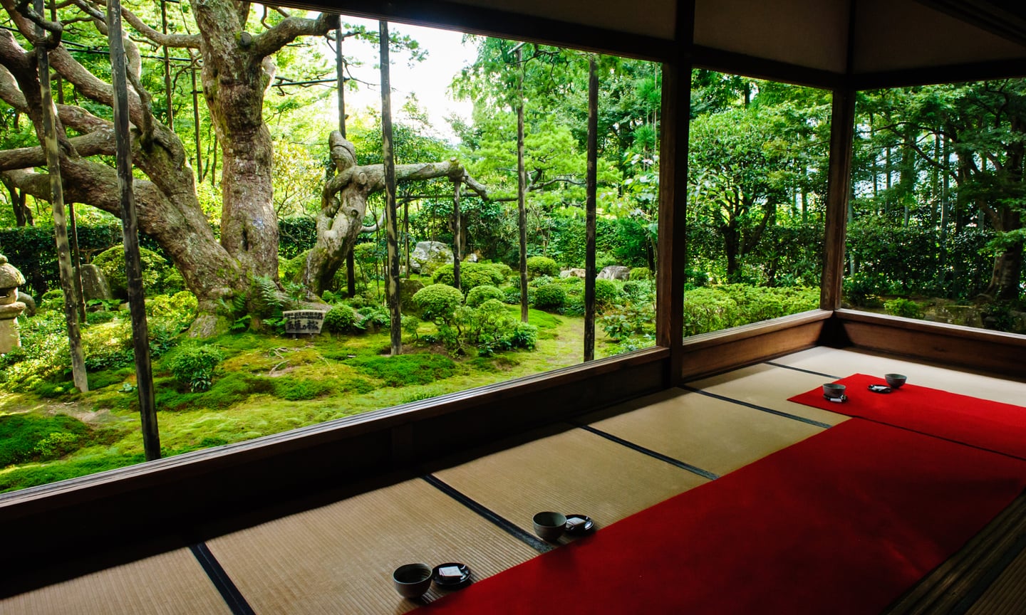 다다미가 깔린 일본식 방 안에서 통창을 통해 바라본 이끼 낀 정원과 울창한 나무들이 어우러진 평온한 풍경입니다.