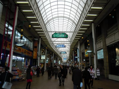 고베 모토마치 상점가, 높은 아치형 천장 아래로 늘어선 화려한 간판들과 쇼핑을 즐기는 사람들의 활기찬 모습입니다.