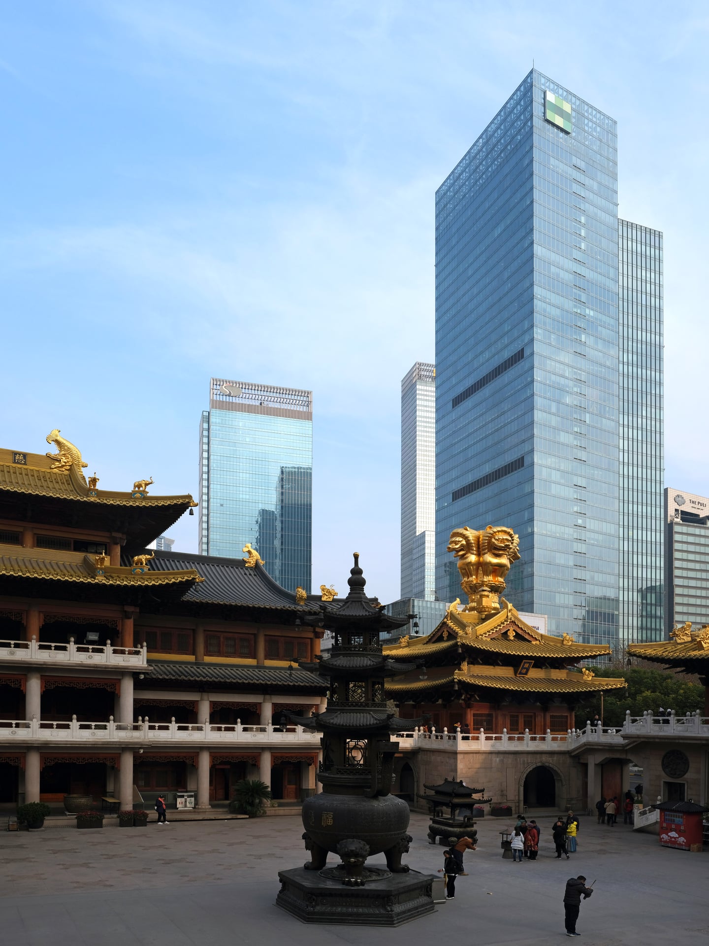 상하이 징안사, 현대적인 유리 외벽의 마천루를 배경으로 화려한 황금 장식의 전통 사찰 지붕과 중앙 향로가 어우러진 도심 속 풍경입니다.