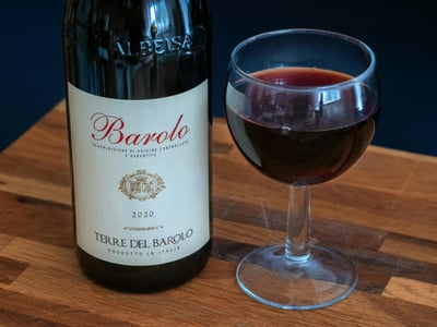 알바 바롤로 와이너리, 나무 테이블 위에 놓인 Terre del Barolo 와인 병과 붉은 루비색 와인이 가득 담긴 우아한 와인 잔의 모습입니다.