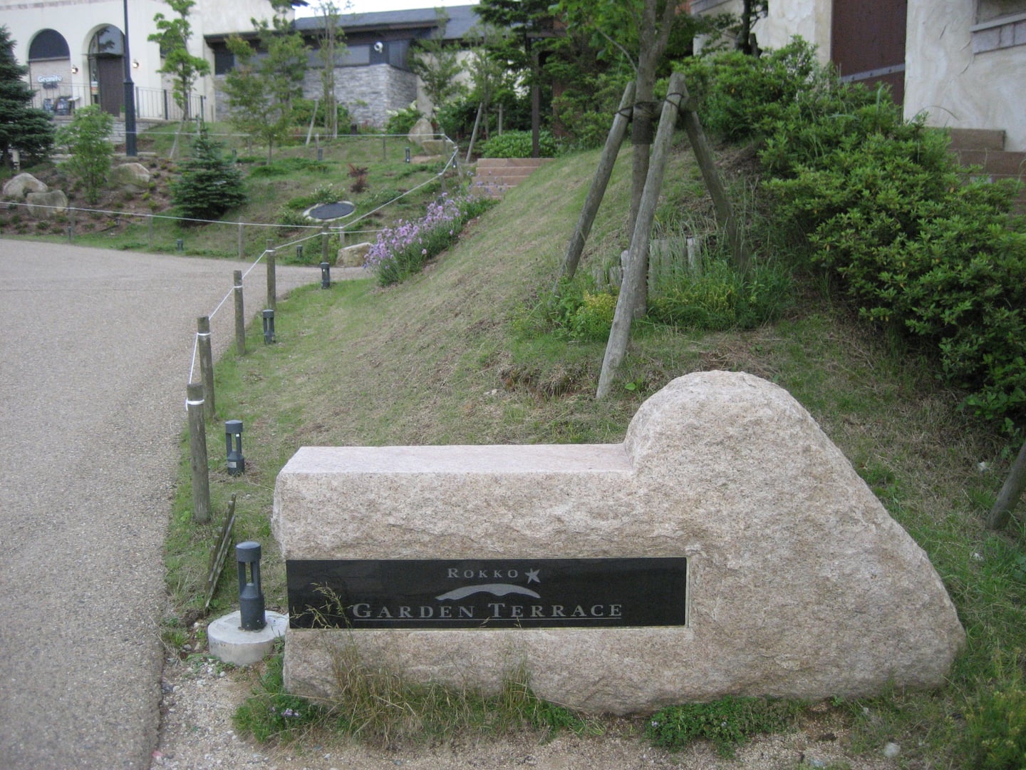 고베 롯코산 가든 테라스, 자연석으로 만들어진 입구 표지석과 푸른 잔디 언덕이 어우러진 평화로운 산책로의 모습입니다.