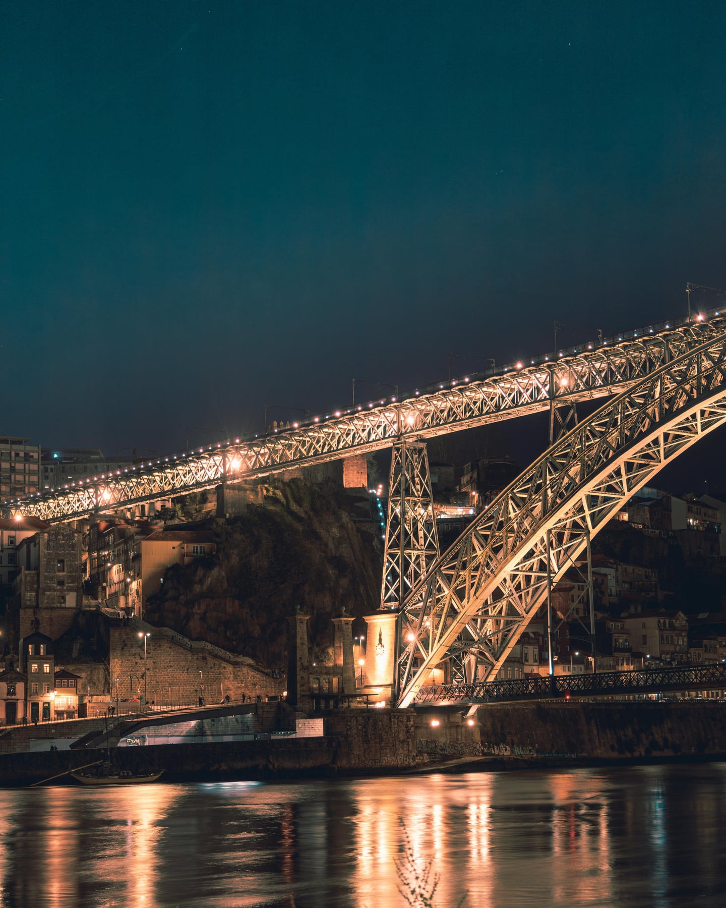 포르투 포르투 야경, 황금빛 조명이 켜진 루이스 1세 다리의 웅장한 철제 구조물과 도루강에 비친 은은한 반영이 어우러진 로맨틱한 밤의 풍경입니다.