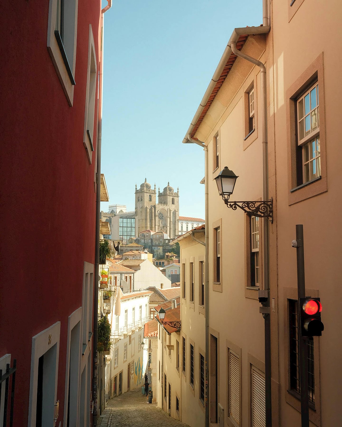 포르투 포르투 구시가지, 좁은 골목길 너머로 보이는 웅장한 포르투 대성당과 따뜻한 햇살이 비치는 고풍스러운 건물들의 조화로운 풍경입니다.